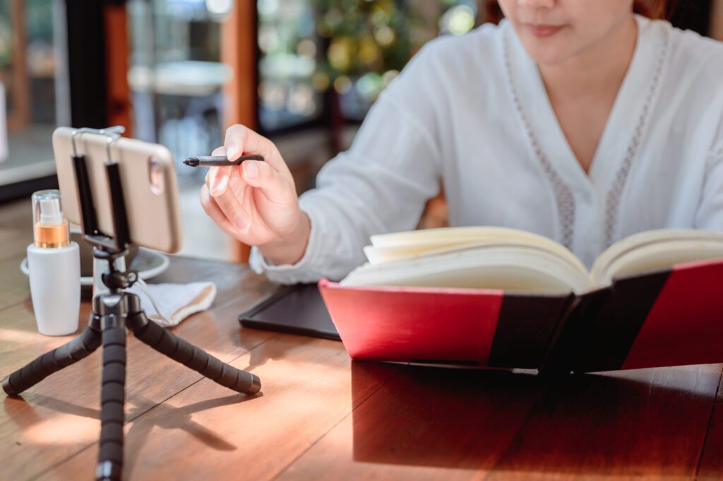 Woman e-learning at home on her phone while reading from a book